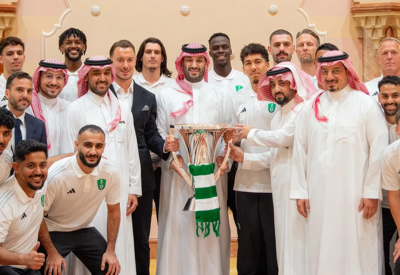 A large group in thobes and team kits gathered around a trophy