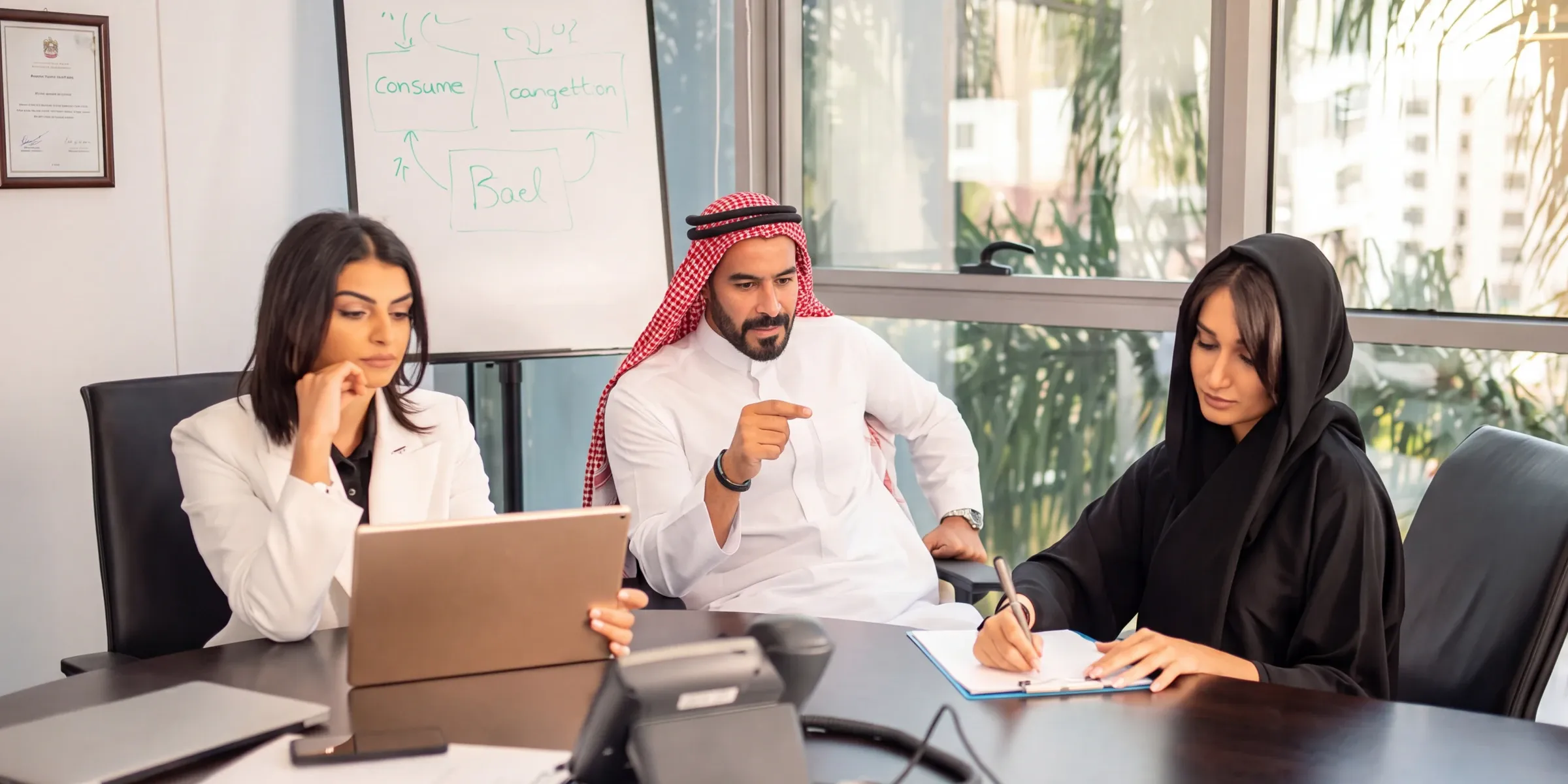 Three government officials in a meeting room, one in a red shemagh pointing at a document